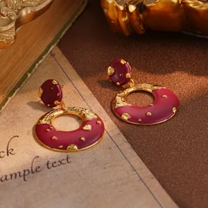 Close-up of vintage burgundy enamel and gold textured round drop earrings on table