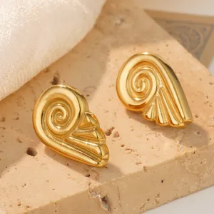 Macro view of golden stainless steel spiral snail earrings on a travertine stone block.