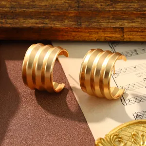 Close-up macro detail of gold vintage C-shaped ribbed hoop earrings on a musical sheet