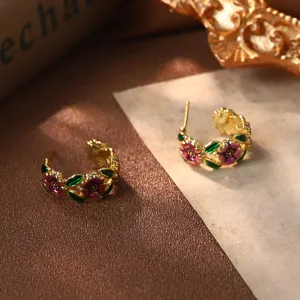 Détail macro de créoles dorées vintage avec fleurs en émail violet et feuilles vertes