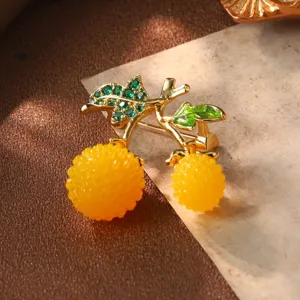 Gros plan d'une broche vintage en forme de fruit avec baies jaunes et feuilles en strass verts