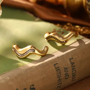 Vue détaillée de boucles d'oreilles vagues dorées avec cristaux sur un vieux livre