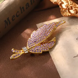 Magnifique broche plume vintage dorée ornée de strass violets étincelants et fins.