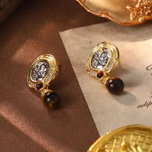 Close-up of vintage gold and silver coin earrings with a dark bead dangle and zircons.