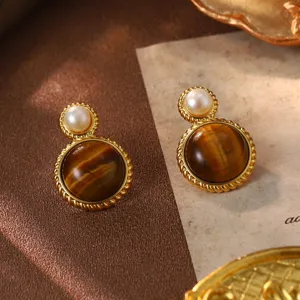 Close-up detail of vintage style gold earrings with tiger eye stones and white pearls.
