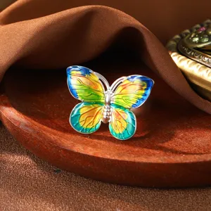 Detaillierte Nahaufnahme eines bunten Emaille-Schmetterling-Ohrrings auf Holztablett