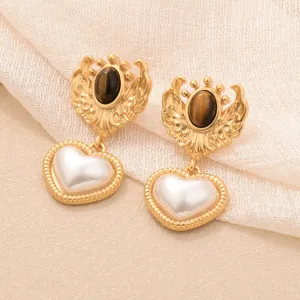 Vue détaillée des boucles d'oreilles vintage cœur perle avec œil de tigre et ailes.