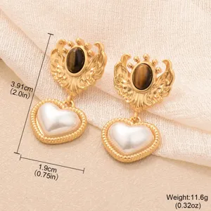 Vue détaillée de boucles d'oreilles vintage dorées avec œil de tigre et cœur perlé