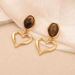 Gros plan de boucles d'oreilles dorées vintage avec pierre oeil de tigre et coeurs