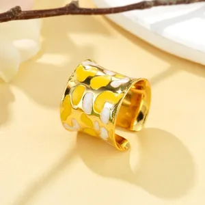 Détail en gros plan d'une large bague ouverte dorée avec motif en émail jaune