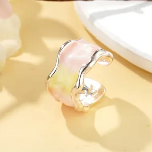 Gros plan d'une bague ouverte en émail rose et jaune avec un anneau métallique argenté.