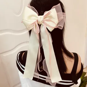Close-up of a large cream and pink ribbon bow hair clip on long black hair.