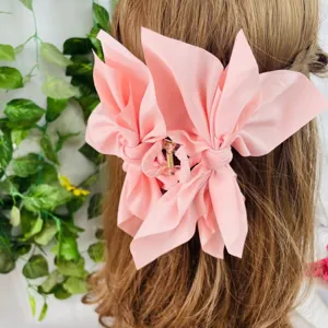 Detailed view of a large pink fabric bow hair claw clip styled on light brown hair.