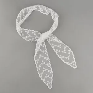 Detailed macro view of a white lace hair ribbon featuring delicate floral embroidery.
