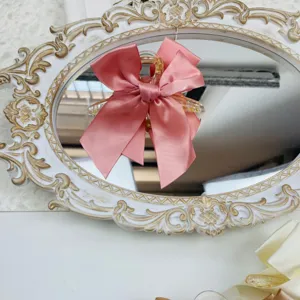 Detailed close-up of a pink satin bow hair claw clip displayed on an ornate vintage mirror tray