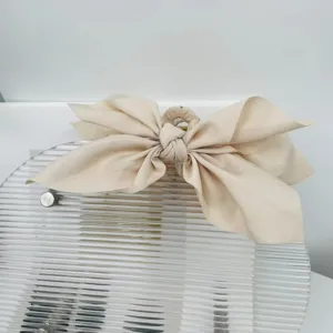 Detailed view of a large beige fabric bow hair claw clip on a modern display stand