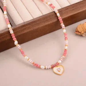 Gedetailleerd zicht op een handgemaakte kralenketting met hartjeshanger en roze stenen op doos