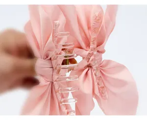 Detailed macro view of a pink fabric bow hair claw clip with clear plastic teeth