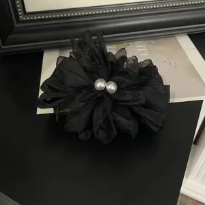 Vista dettagliata di una grande molletta per capelli a fiore in tessuto nero con perle