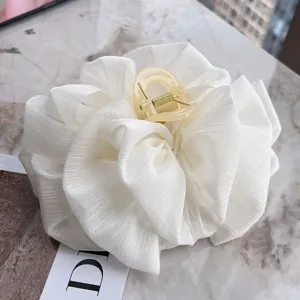 Detail of white pleated cloud bow hair claw clip on marble surface.