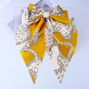 Detail of a large yellow floral bow hair clip with long silky ribbon tails.