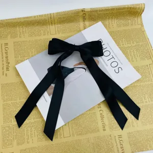 Detail view of a large black satin ribbon bow hair clip on vintage newspaper.