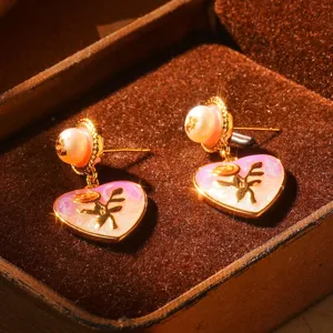Vue détaillée des boucles d'oreilles en émail vintage en forme de cœur avec perles et ange doré.