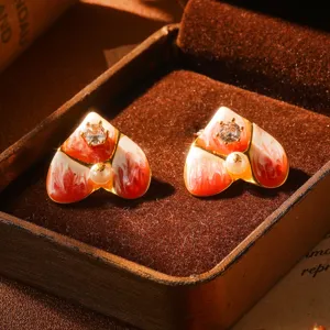Gros plan de boucles d'oreilles cœur en émail français avec détails perles et oxydes.