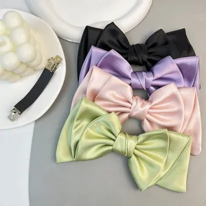 Close-up of elegant satin bow hair clips in black, purple, pink, and green, showing smooth texture.