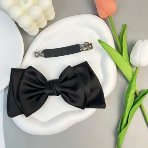 Macro view showing the elegant black satin texture and sturdy metal clip of the bow hair pin