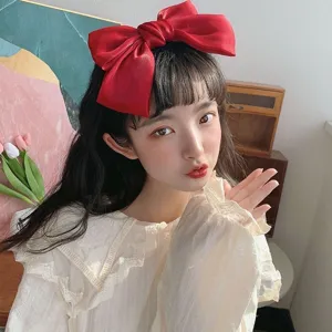 Detail view of a large red silk bow hair clip worn by a model in a lifestyle setting