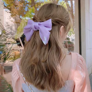 Macro detail of a shiny lavender silk bow hair clip styled on elegant wavy brown hair