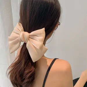 Back view of an oversized champagne shiny silk bow hair clip on model's tied hair.