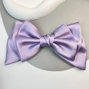 Detailed macro shot of a large purple satin bow hair clip with glossy silk texture.