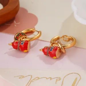 Close-up of golden hoop earrings with red enamel gourd charms