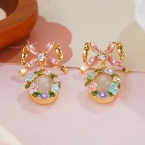 Close-up detail of pink enamel bow earrings with floral accents and faux pearl center