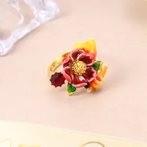 Detailed macro view of the red enamel flower and red gemstone on a golden adjustable ring.