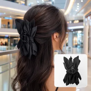 Large black fabric bow hair claw clip shown on a woman's hair with product close-up