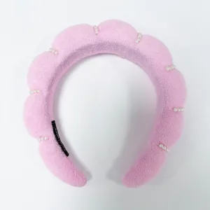 Vista detallada de una diadema de esponja rosa con elegantes detalles de perlas blancas.