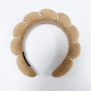 Vista detallada de una diadema acolchada de esponja marrón con pequeñas perlas blancas