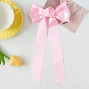 Detail of pink satin bow hair clip with central rose flower and long ribbons