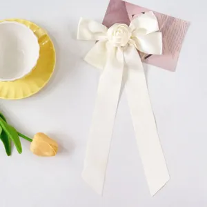 Detail of handmade cream satin ribbon bow hair clip with a central fabric rose accent.