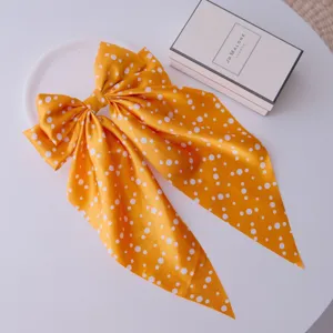 Detailed view of yellow polka dot bow hair clip with long ribbons on white surface