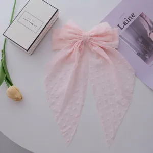 Elegant macro detail of a pink chiffon dot ribbon large bow hair clip on a white table
