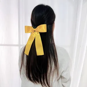 Back view of a yellow satin bow hair clip with long streamers worn on dark hair.