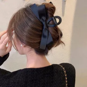 Close-up of elegant black ribbon bow claw clip styling a low bun on brunette hair.