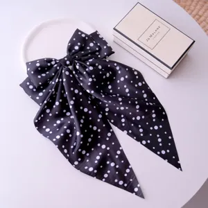 Macro detail view of black polka dot fabric hair bow clip with long silky ribbons