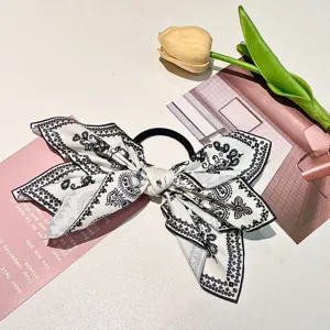 Close-up of a large black and white paisley print fabric bow hair tie on white surface
