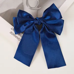 Close-up of navy blue satin bow hair clip with long ribbon tails on white background