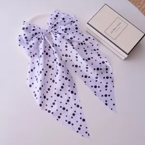 Polka dot bow hair clip with streamers presented elegantly beside a branded gift box.